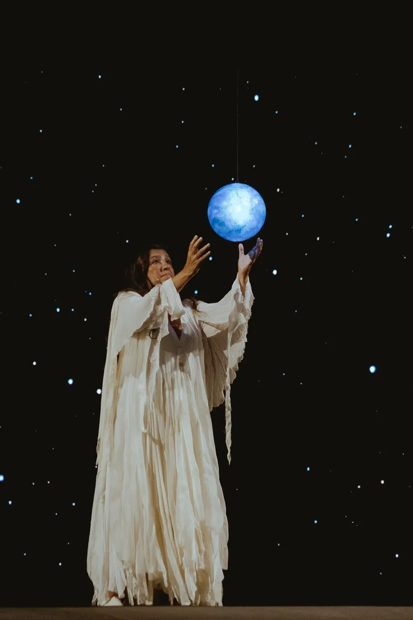 Atriz Regina Casé, de roupa longa branca segurando uma bola azul na peça Viva! Vida! Foto: Ariel Cavotti